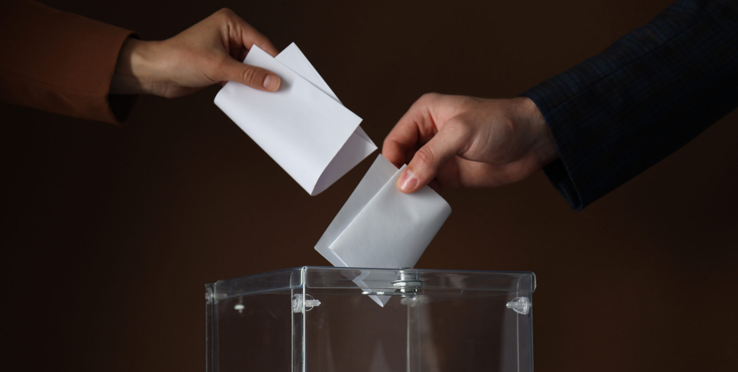 Transparent box and hands with voting papers on brown background